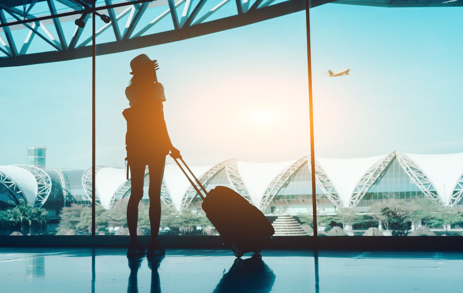 Traveller with a suitcase watching a plane take off at the airport